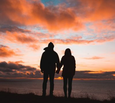 a couple of people standing on a beach at sunset